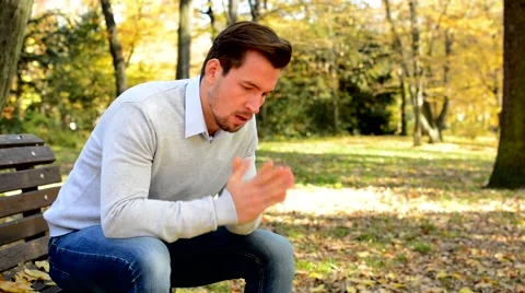 Young man sits on bench in a park, is nervous, sad and thinks Stock Footage 59725842