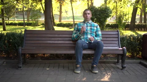A young man sits on a bench in the park and drinks cold coffee closeup. In the Stock Footage 140112972
