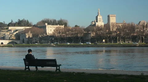 Young man sits on a bench at Rhone river with Avignon in the bg Stock Footage 62481304