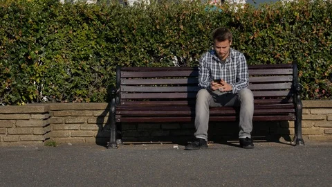 Young man sits on a bench using a phone to text Stock-Footage 97018143