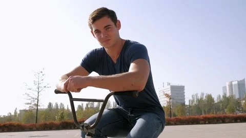 A young man sits on a BMX Bicycle in a Park in Sunny weather. Stock Footage 231540662