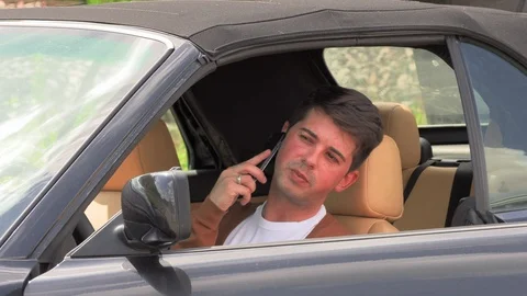 A young man sits in a broken car and makes phone calls 库存影片 113223943