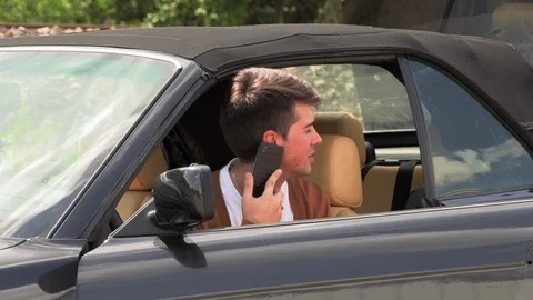 A young man sits in a broken car and makes phone calls 動画素材 113225774