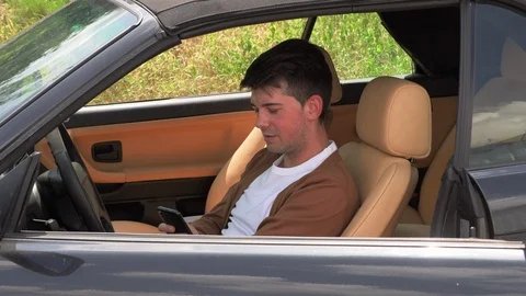 A young man sits in a broken car and makes phone calls Stock Footage 113226538
