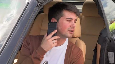 A young man sits in a broken car and makes phone calls Видео 113389088
