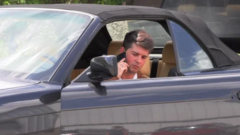 A young man sits in a broken car and makes phone calls 库存影片 113389234