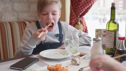 A young man sits in a cafe and eats sushi with sticks. A dish of traditional 库存影片 87400897