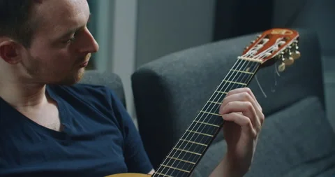 A young man sits on the couch and plays the guitar. Close-up portrait of a man Stock Footage 147152186