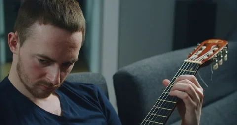A young man sits on the couch and plays the guitar. Close-up portrait of a man Stock-Footage 147221249