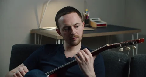 A young man sits on the couch and plays the guitar. Close-up portrait of a man Stock Footage 147221601