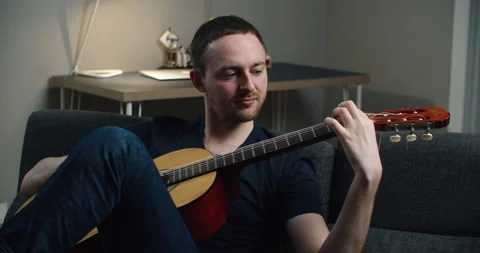 A young man sits on the couch and plays the guitar. Close-up portrait of a man Stock Footage 147952254