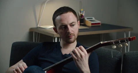 A young man sits on the couch and plays the guitar. Close-up portrait of a man Stock Footage 147952650