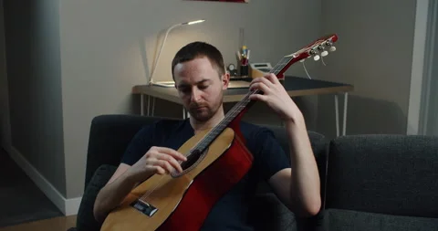 A young man sits on the couch and plays the guitar. Close-up portrait of a man Stock Footage 147982579