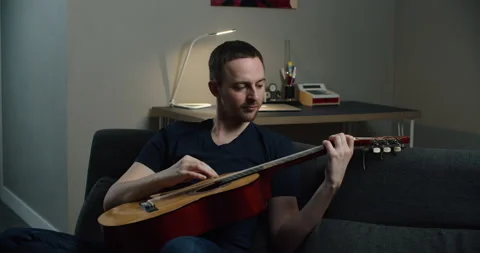 A young man sits on the couch and plays the guitar. Close-up portrait of a man Stock Footage 148315020