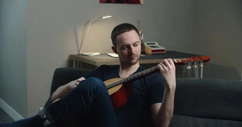 A young man sits on the couch and plays the guitar. Close-up portrait of a man Stock Footage 148501959