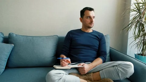 A young man sits on the couch and takes notes in a notebook Stock Footage 169302770