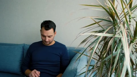 A young man sits on the couch and chatting on the phone Stock Footage 169302983