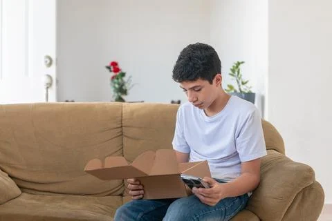 A young man sits on a couch, looking at his phone Stock Photos