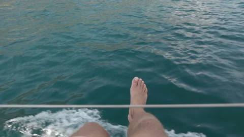 Young man sits on the deck of a moving yacht and swinging his legs in the air Stock Footage 107496081