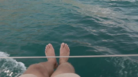 Young man sits on the deck of a moving yacht and swinging his legs in the air Stock Footage 107496995