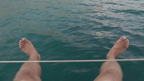 Young man sits on the deck of a moving yacht and swinging his legs in the air Stock Footage 107497734