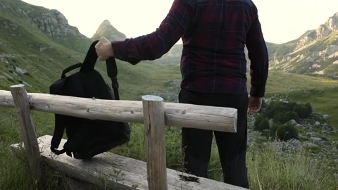 A young man sits down on a bench at a viewpoint in a mountain valley. Stock Footage 247975875