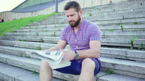 Young man sits down on stairs and starts reading newspaper. 動画素材 67608147