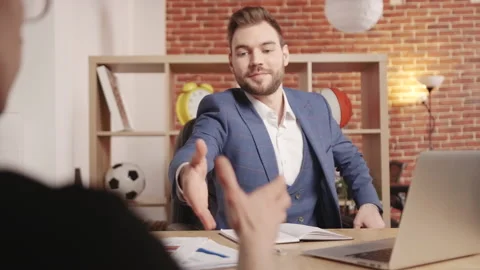 A young man sits down at the table and shakes hands with a colleague against 動画素材 194363383