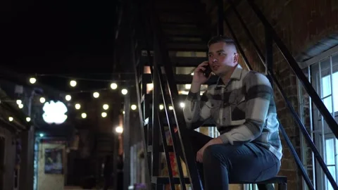 A young man sits on a fire escape and talks on the phone. A man on the stairs of 스톡 동영상 253801847