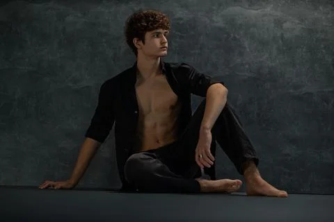 Young man sits on the floor in a studio dressed in a black shirt with an open Fotos de archivo