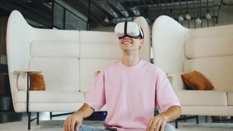 Young man sits on the floor wearing virtual reality headset while looking around Stock Footage 330688821