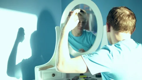 Young man sits in front of a mirror and sprays perfume on himself Stock Footage 128463865