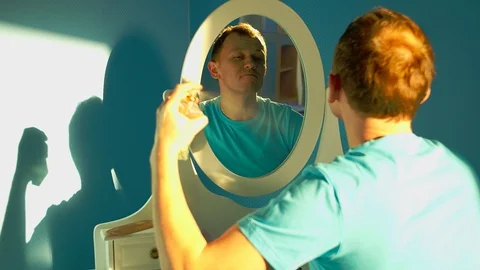 A young man sits in front of a mirror and sprays perfume on himself Stock Footage 129381674