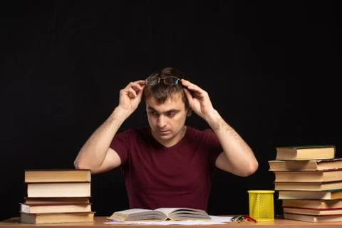 A young man sits in front of an open book at the table. Stock Photos