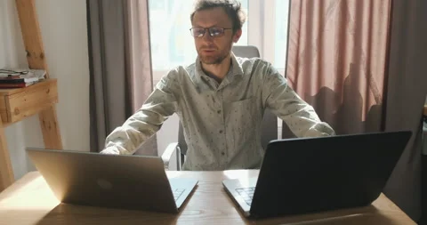 Young man sits in front of two laptops in his home office and has a video chat Vídeo Stock 202083038