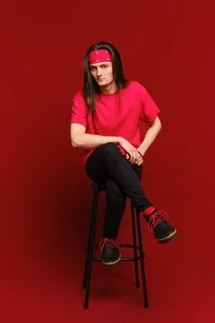 Young man sits on high stool with his leg on another leg and leaning forward Foto stock