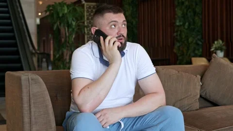 A young man sits on a hotel sofa and talks on the phone Stock Footage 334377064