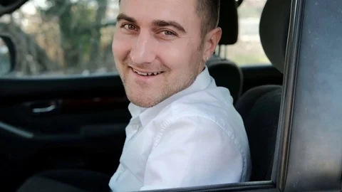 Young man sits inside parked car and smiles Video stock 74694364