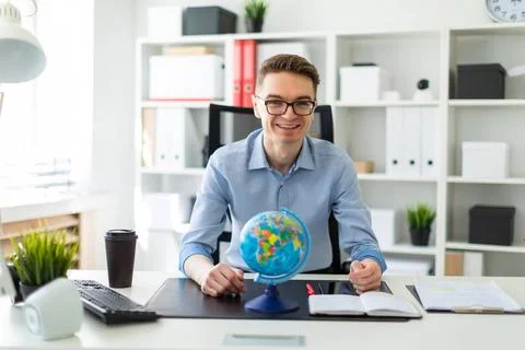 A young man sits in the office at a computer desk and in front of him stan... Stock-Fotos