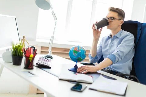 A young man sits in the office at a computer desk, holds a globe with his ... Stock-Fotos