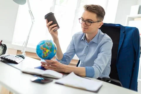 A young man sits in the office at a computer desk and holds a glass of cof... Stock-Fotos