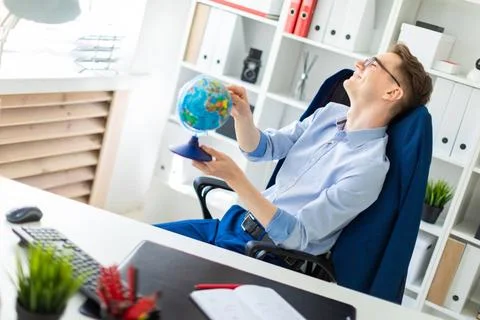A young man sits in the office at the computer desk, closes his eyes and p... Stock-Fotos