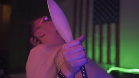A young man sits in a semi-lit room with neon lighting and smokes a hookah Stock Footage 130126318