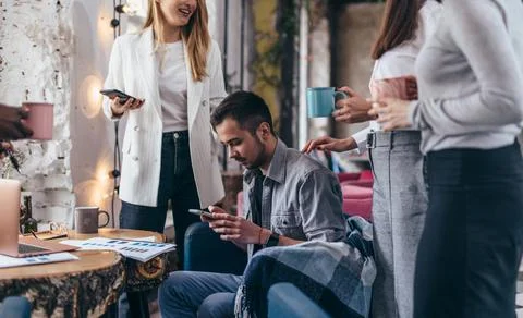 Young man sits with a smartphone while his colleagues talk Stock Photos