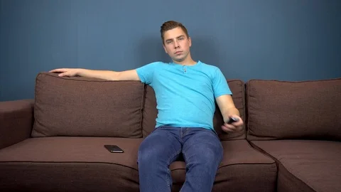 A young man sits on a sofa and watches TV. The view from the TV. Looking at the Video stock 118489056