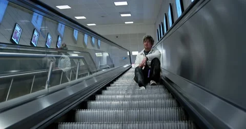 A young man sits on the steps of an escalator in the subway. Underground passage Stock Footage 237400416