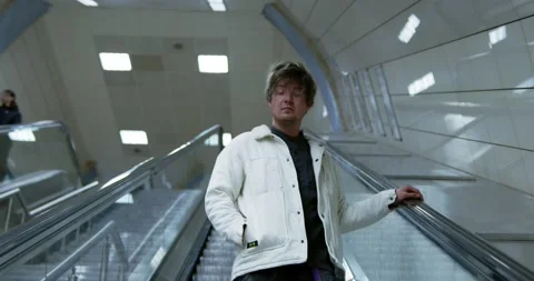 A young man sits on the steps of an escalator in the subway. Underground passage Stock Footage 237400462
