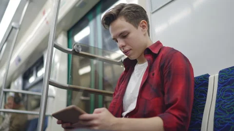 A young man sits on a subway train and looks at something on a pocket computer. 스톡 동영상 209213567