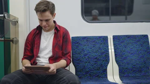 A young man sits in a subway train and plays a game on a pocket computer. Stockbeeldmateriaal 209218030
