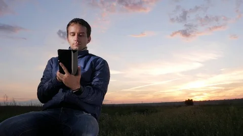 A young man sits at sunset and checks the messages to check the messages on the Stock Footage 76922268